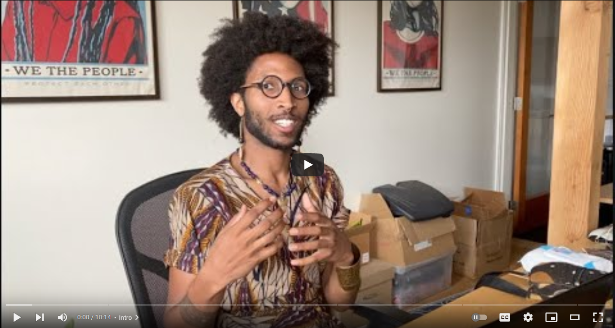 YouTube player showing Paris Chapman, animatedly speaking to the camera at a desk in front of vibrant illustrated posters