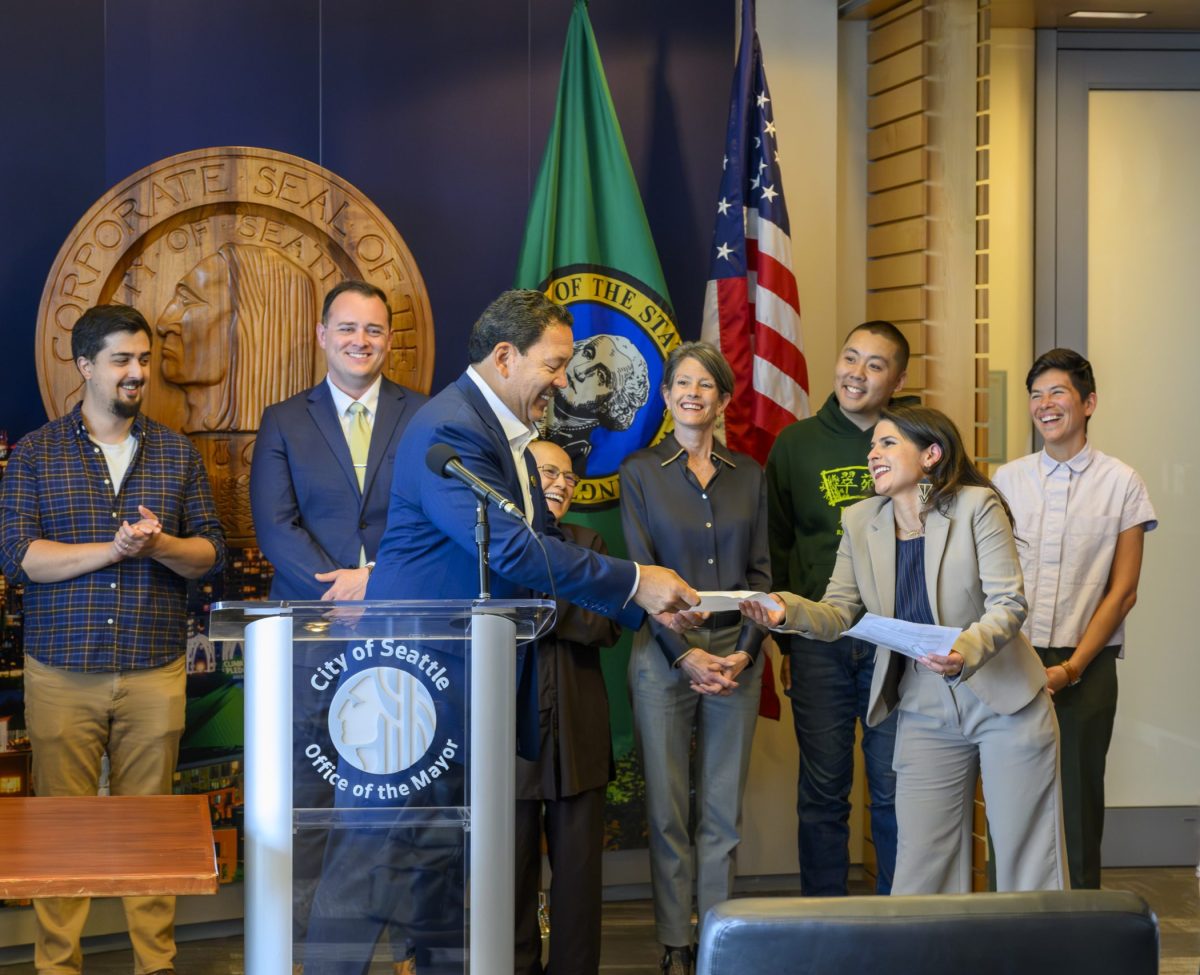 The Mayor of Seattle, City Councilmembers, and non-profit and small business leaders smile and stand together.