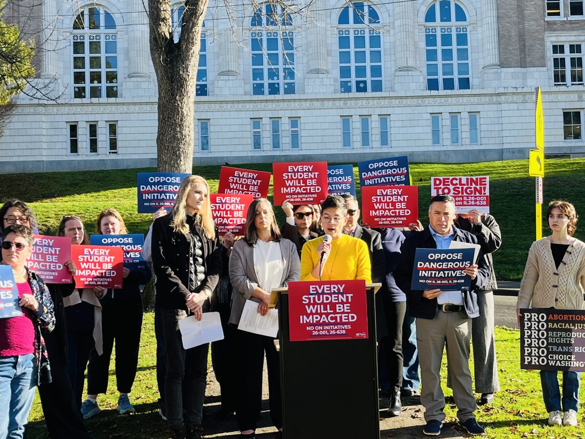 CEGV Co-ED speaks at a podium with a group of supporters standing behind her